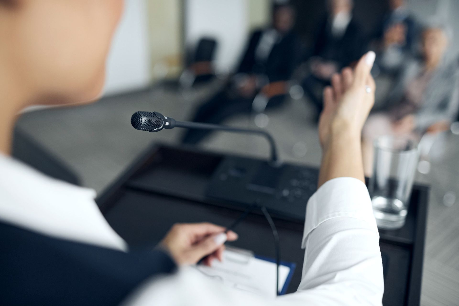 A speaker at a lectern microphone addresses an audience during a press briefing